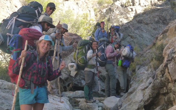 a group of people wearing backpacks smile while standing on a rocky landscape